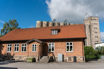 An old one-story house from red bricks in front of a huge grain elevator