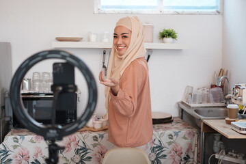 Mature Muslim woman in hijab preparing vegetable salad in kitchen while live streaming online. Vegan vegetarian food concept.