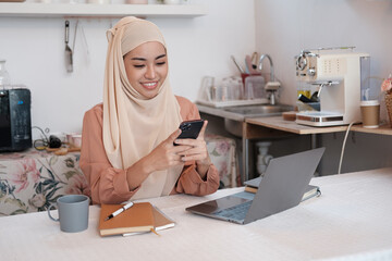 Young pretty modern muslim woman in hijab working on laptop in office room, education online, remote work freelancer, using smartphone