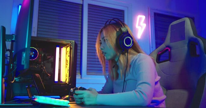 Game over you lose. Angry Asian gamer wearing gaming headphones playing joystick console video game on computer PC neon light at home feeling sad disappointed about game losing, player unhappy E-Sport
