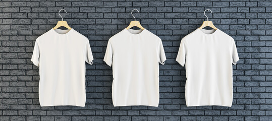 Three empty white t-shirts hanging on black brick wall background. Ad, textile and fashion concept....