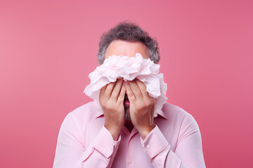 Runny nose background. Man blowing night in handkerchief isolated on pink background. Seasonal cold or flu and sinus theme.generative ai
