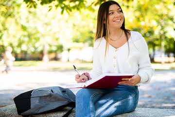 Beautiful female college student reading a book on a bench in a park