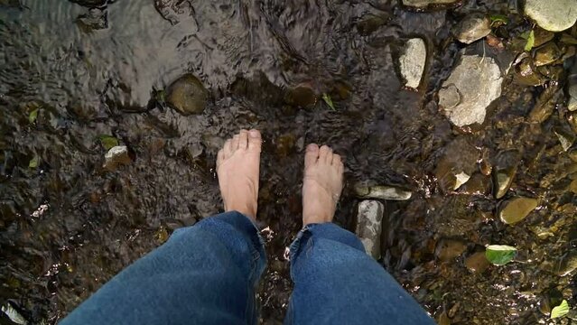 Woman's legs in the river water stream. Slow motion. Rewilding, mental health retreat concept.