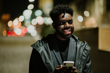 Portrait of a young urban African American man using his phone on a city street at night.