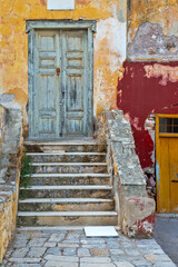 Entrance of a beautiful old house with bright though aged colors on worn offs walls, in Hydra island, Greece, Europe.
