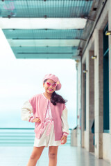 Retrato de linda niña coqueta con atuendo rosa y gafas de sol rosa en el muelle