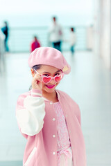 Retrato de linda niña coqueta con atuendo rosa y gafas de sol rosa en el muelle