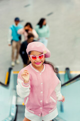 Retrato de linda niña sonriente con atuendo rosa y gafas de sol rosa en la ciudad