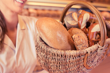 sales woman in bakery shop presenting a basket with bread and rolls
