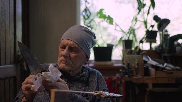 Elderly male master works in his workshop restoring japanese deba knife sheath