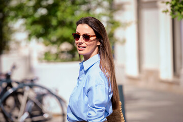 Attractive brunette haired woman wearing sunglasses and walking on the street