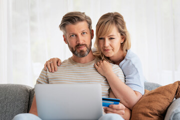 Middle-aged couple wearing casual clothes and sitting at home on the sofa and shopping online