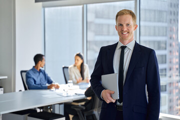 Smiling young business man corporate team leader standing in office. Confident businessman manager, male executive wearing suit and tie standing in office with team workers at meeting room, portrait.