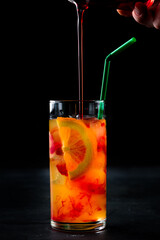 Alcoholic cocktail Tequila Sunrise with orange slices with pouring syrup.