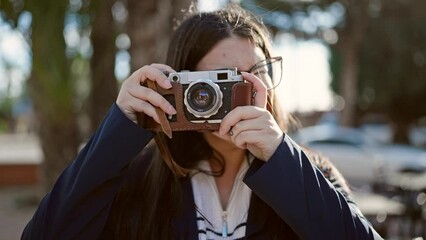 Young hispanic woman tourist wearing backpack taking pictures with camera at street