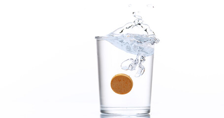 Tablet or Vitamin Falling and Dissolving into a Glass of Water against White Background