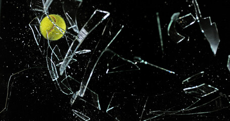 Tennis Ball breaking Pane of Glass against Black Background