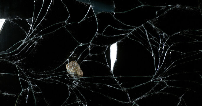 Stone breaking Pane of Glass against Black Background
