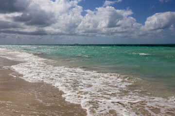 Waves breaking on a sand, view to ocean beach and sky with white clouds. Background for holidays on a paradise nature