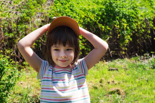 Happy child in a cap outdoors on a sunny warm day looks to the side. Carefree time, freedom and tranquility.