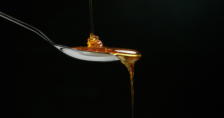 Honey Flowing in a spoon against Black Background