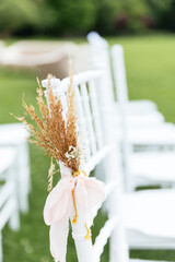 White chairs lined up for an event accompanied by a bouquet of boho flowers. Chairs for wedding ceremony. Beautiful wedding flower decorations. Outdoor wedding ceremony. 
