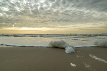 windy beach, sea foam and low clouds at sunset
