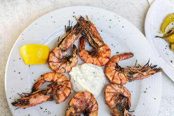 Grilled shrimps with yoghurt tzatziki sauce, lemon and herbs on white plate for a dinner - mediterranean greek cusine