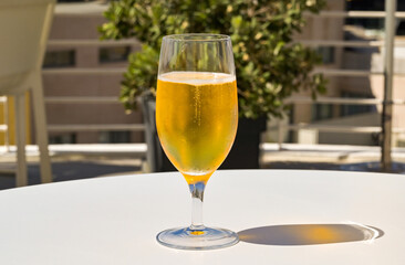 Close up view of a glass of chillded golden colour lager beer on a table on the outdoor terrace of a hotel bar. No people.