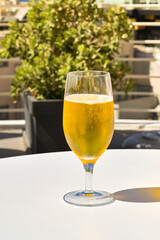 Close up view of a glass of chillded golden colour lager beer on a table on the outdoor terrace of a hotel bar. No people.