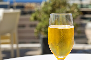 Close up view of a glass of chillded golden colour lager beer on a table on the outdoor terrace of a hotel bar. No people.