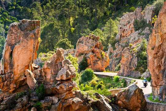 Motobiker on road among the rocks of Calanche de Piana, Les Calanques de Piana in Corsica, France