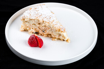 Slice of classic layer cake Napoleon with custard, powdered sugar and strawberries on plate.