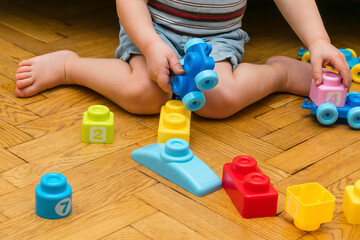 Cute little adorable caucasian boy playing with multi-colored constructor at home. Babys hands...
