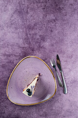 Piece of cake with fresh blueberries and vanilla cream on a purple background.