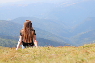 The concept of relaxation, tourism and recreation. A trip to the Carpathians, Ukraine. View from the back of a girl sitting on the grass in front of a mountain landscape, nature
