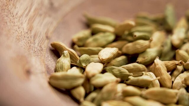 Dry cardamon spicy pods falling in slow motion into a wooden bowl closeup with rotation