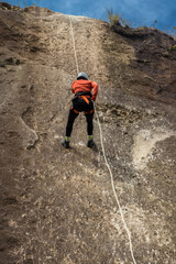 vertical shot of young sporty woman rappelling over rock wall wearing helmet and harness ropes in Costa Rica
