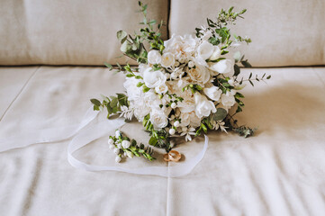 Wedding accessories and details, gold rings, a bouquet of flowers with a ribbon lie on a beige sofa. Close-up photography, portrait.