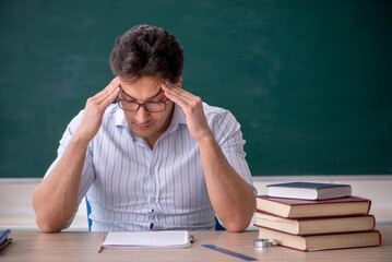 Young male teacher in front of green board