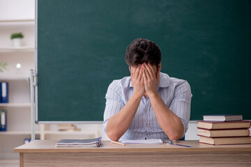Young male teacher in front of green board