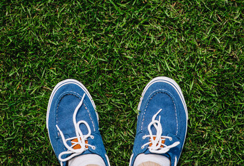 A man in blue denim shoes, sneakers stands on green grass in a meadow. Photography, top view, lifestyle.