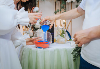The bride and groom pour layers of colored kinetic sand into a glass bowl on the table, conducting...
