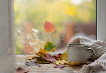 Cozy autumn concept. A cup of tea on a windowsill against a background of glass with raindrops