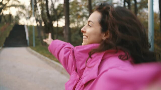 Smiling young lady making video on phone while enjoying of walk in the park outdoors. Seasonal style, autumn season. Positive emotion concept. Slow motion