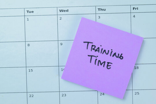 Concept of Training Time write on sticky notes with calendar isolated on Wooden Table.