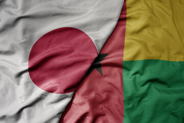 big waving national colorful flag of japan and national flag of guinea bissau .