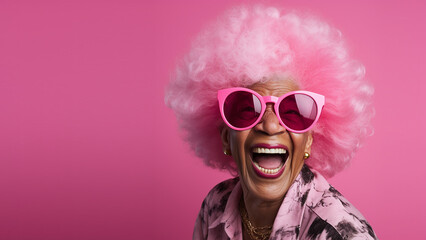 Happy, laughing, lovely old woman, with pink afro hair and pink sunglasses, on solid colour background, with room for text.