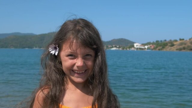 A child with a flower in her hair.a. Portrait of a happy little girl at the sorch with a flower in her hair.